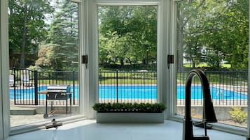 A room with a view of a swimming pool, a grill, and a potted plant.