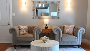 A room with two tufted sofas, a round coffee table, a mirror with a decorative frame, and a lamp.