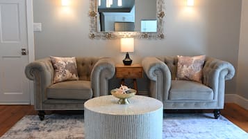 A room with two tufted sofas, a round coffee table, a mirror with a decorative frame, and a lamp.