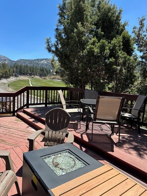 Eine Terrasse mit Gartenmöbeln, einer Feuerstelle und Blick auf einen Golfplatz und Berge.