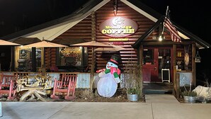 Un bâtiment de style chalet en rondins, avec une enseigne indiquant « Moonridge Coffee Company », une décoration représentant un bonhomme de neige et une véranda en bois avec des chaises rouges.