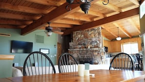 Un coin repas avec une table en bois, des chaises, une cheminée en pierre et un téléviseur fixé au mur.