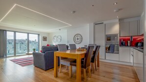 A modern living room with a dining table, grey sofa, and city view. - Square Green (No 15) | Balcony (St Andrews)
