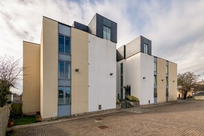 A modern building with a flat roof, large windows, and a paved courtyard.