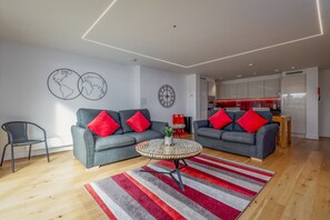 A modern living room with two grey sofas, red cushions, a round coffee table, and a striped rug.