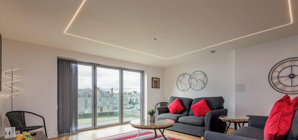 Ein modernes Wohnzimmer mit einer Couch, einem Couchtisch und einem großen Fenster mit Blick auf Gebäude.