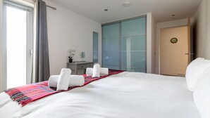 A hotel room with a large bed, a desk, a chair, and a window with curtains. - Square Green (No 15) | Balcony (St Andrews)