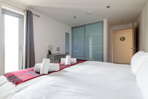 Una habitación de hotel con una cama grande, un escritorio, una silla y un ventanal con cortinas.
