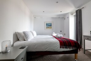 A modern hotel room with a neatly made bed, a bedside table with a lamp, a desk with a chair, and a window with curtains.