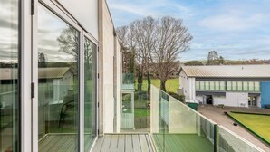 A modern building with large glass windows, a balcony, and a view of a green field and trees. - Square Green (No 15) | Balcony (St Andrews)