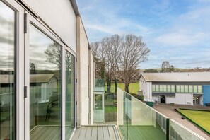 Ein modernes Gebäude mit großen Glasfenstern, einem Balkon und Blick auf ein grünes Feld und Bäume.