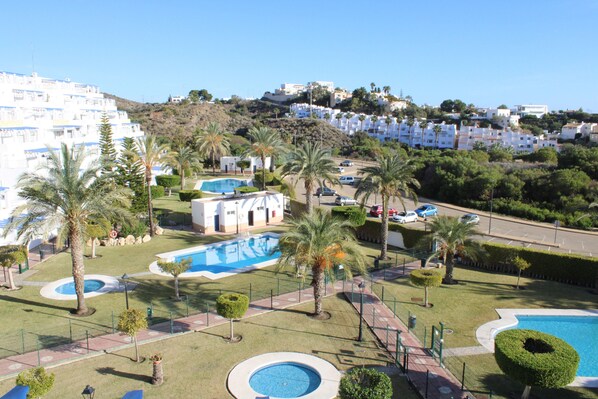 A residential area with a swimming pool, palm trees, and a hilly backdrop. - 2 Bedroom Apartment (MOJACAR)