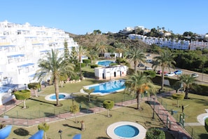A resort with multiple swimming pools, palm trees, and a hillside view. - 2 Bedroom Apartment (MOJACAR)