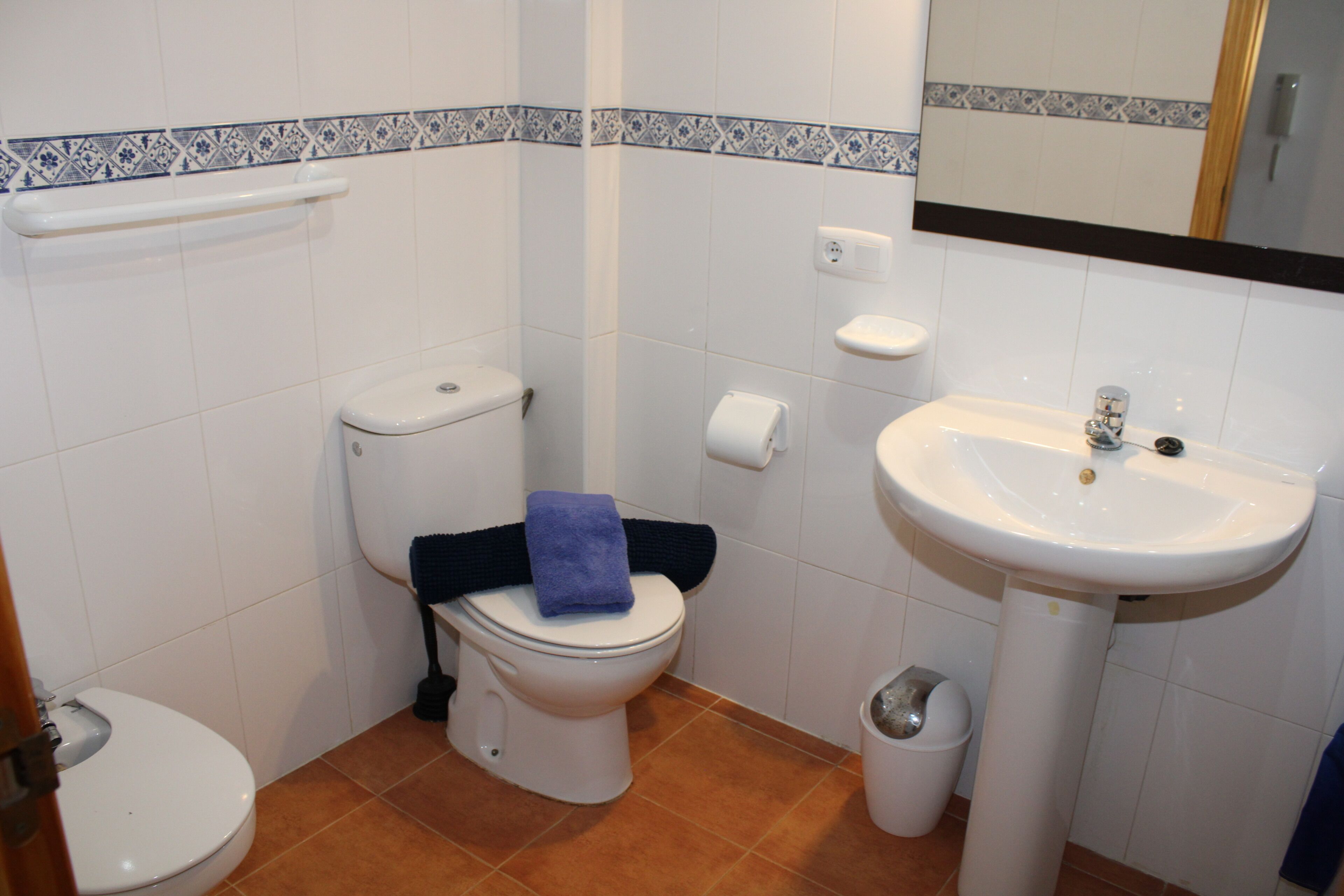 A bathroom with a toilet, sink, and a trash bin.