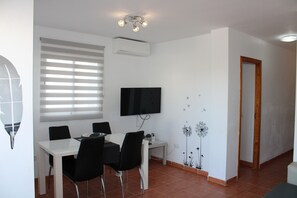 A dining area with a white table, black chairs, a flat-screen TV, and a window with blinds. - 2 Bedroom Apartment (MOJACAR)