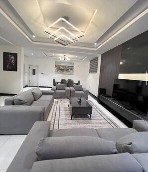 A modern living room with grey sofas, a coffee table, and a flat-screen TV. - Dahila Apartment By Feenixkoncepts (Abuja)