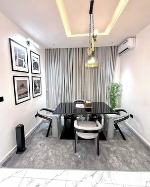 A modern conference room with a black table, grey upholstered chairs, a chandelier, and framed pictures on the wall. - Dahila Apartment By Feenixkoncepts (Abuja)