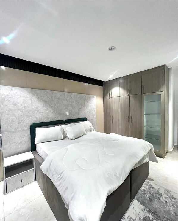 A modern bedroom with a large bed, built-in wardrobe, and a marble headboard. - Dahila Apartment By Feenixkoncepts (Abuja)