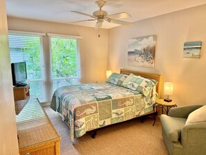 Ein Schlafzimmer mit einem Bett, einem Fernseher, einem Sessel, einer Lampe und einem Deckenventilator.