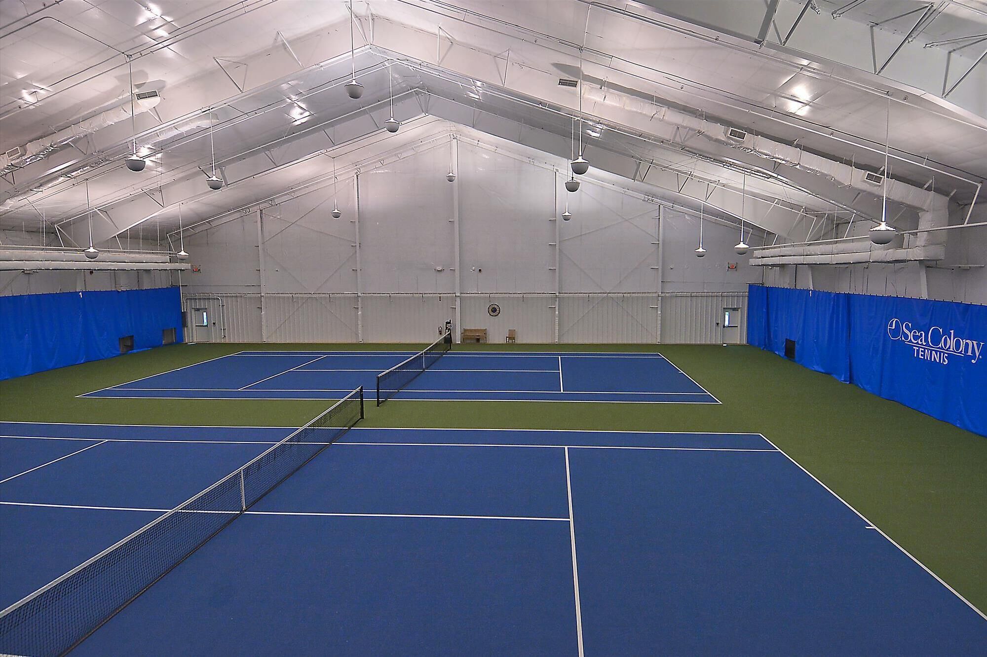 Un complexe de tennis intérieur doté de plusieurs courts, de hauts plafonds et d’un éclairage artificiel.