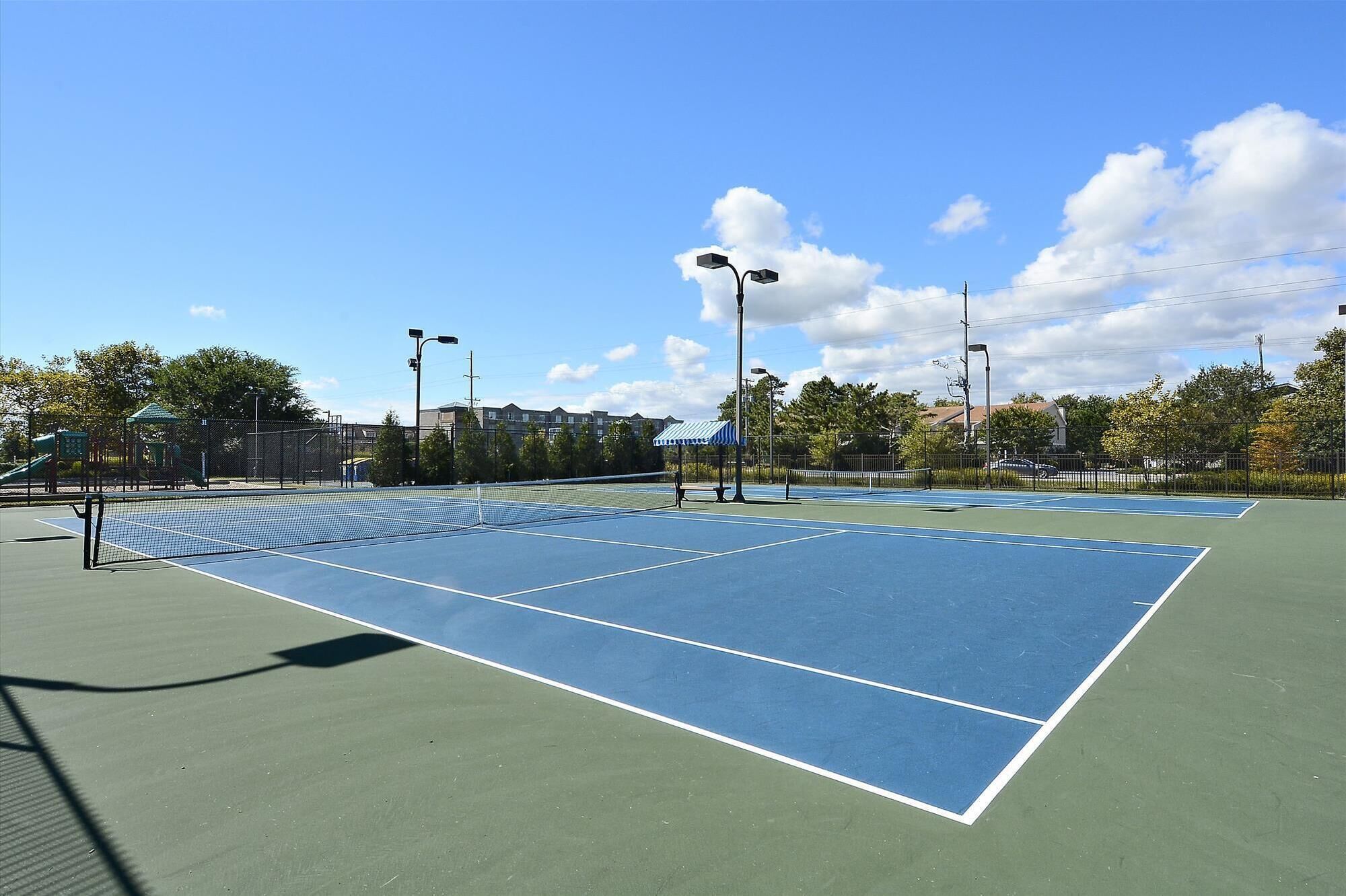 Un court de tennis en plein air, doté d’un filet et entouré d’arbres et d’immeubles.