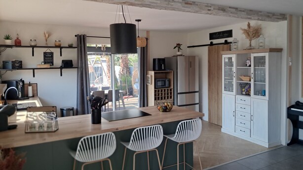 Una cocina moderna con una isla central, taburetes de bar, microondas integrado y refrigerador.