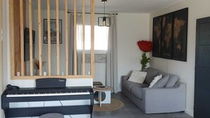 Una sala de estar con un piano, un sofá, una mesita redonda y una planta decorativa.