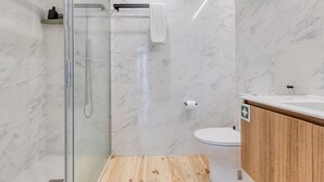 A modern bathroom with a glass shower enclosure, a wooden vanity, and a marble-tiled wall. - FindMe inPorto Bonfim 0F (Porto)