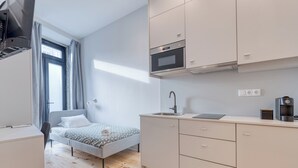 A compact bedroom with a bed, a bedside table, and a window with curtains. Adjacent is a kitchenette with a sink, a microwave, and a coffee machine. - FindMe inPorto Bonfim 0F (Porto)