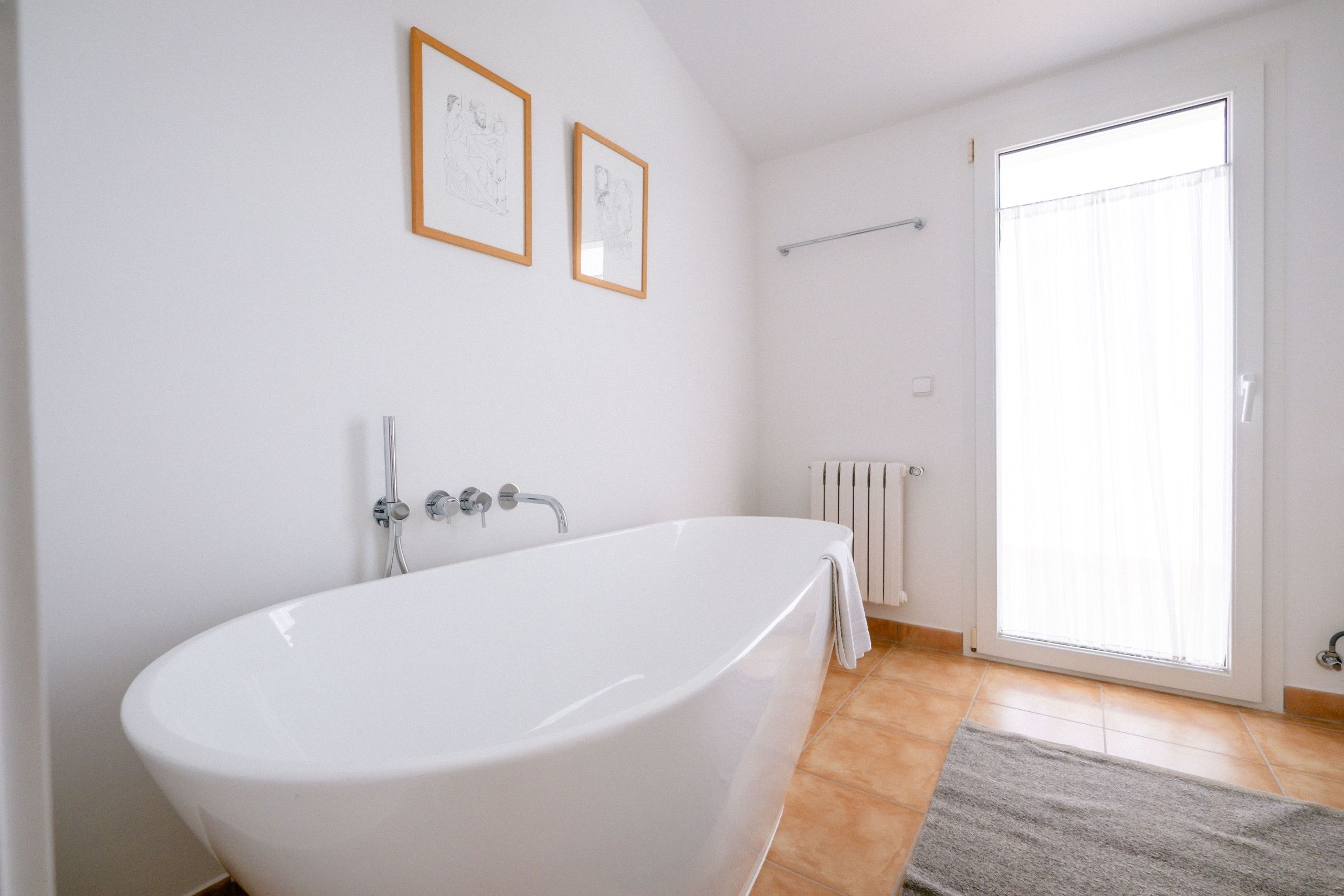 A bathroom with a freestanding bathtub, a towel rack, a radiator, and a window with blinds.