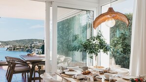Een eetruimte met uitzicht op zee, een gedekte tafel met borden en glazen, en een hanglamp.