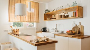 Een keuken met een houten kookeiland, witte kasten, een raam met zonwering en een plank met keukengerei.