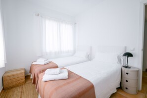 Ein Hotelzimmer mit zwei Betten, einem Nachttisch mit Lampe und einem Fenster mit transparenten Vorhängen.