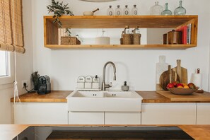 A kitchen with a white sink, wooden shelves above, and a countertop with various items. - Casa Barbara - Harbor view (Es Castell)
