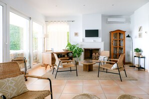 A spacious living room with a fireplace, comfortable seating, and a large window. - Casa Barbara - Harbor View (Es Castell)