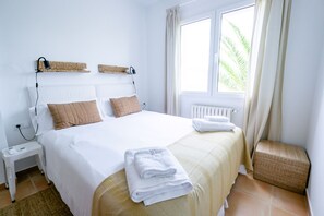 A hotel room with a bed, bedside tables, a window with curtains, and a view of palm trees. - Casa Barbara - Harbor View (Es Castell)