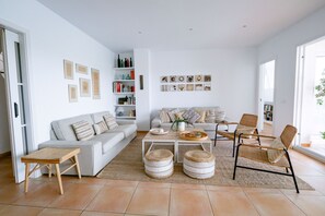 A spacious living room with a sofa, coffee table, and chairs. There are bookshelves and artwork on the walls. - Casa Barbara - Harbor view (Es Castell)