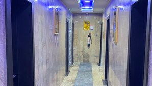 Un pasillo con suelo de baldosas azules, puertas de ascensor negras e iluminación azul en el techo.