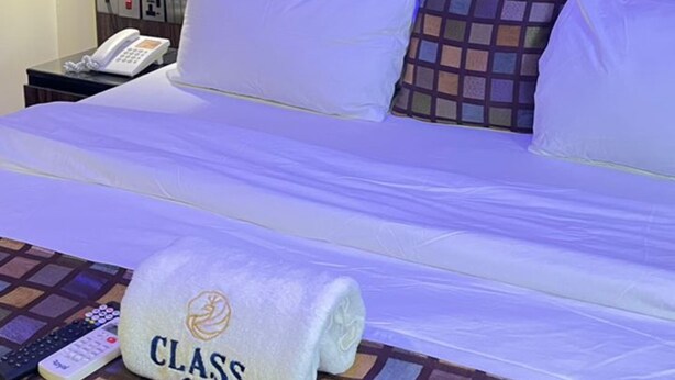Habitación de hotel con cama, mesita de noche con teléfono y toalla con la palabra 'CLASS'.