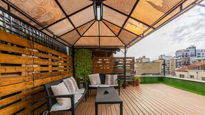 Une terrasse sur le toit avec un plancher en bois, une table noire, deux chaises en osier noir, un mur vert et un plafond à motifs.