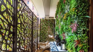 A room with a decorative black metal partition, a green vertical garden, a wicker chair, and a small table with a lantern. - ISLAND GARDEN DESIGN HOUSE (Milano)