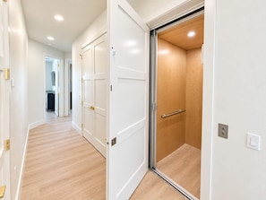 A hallway with white doors, a wooden floor, and an elevator with a glass door. - Drift House · 2026 Luxury 6 King Suites Boat Dock (Fort Myers Beach)