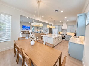 A modern kitchen with a central island, pendant lighting, and a dining area with a wooden table and chairs. - Drift House · 2026 Luxury 6 King Suites Boat Dock (Fort Myers Beach)