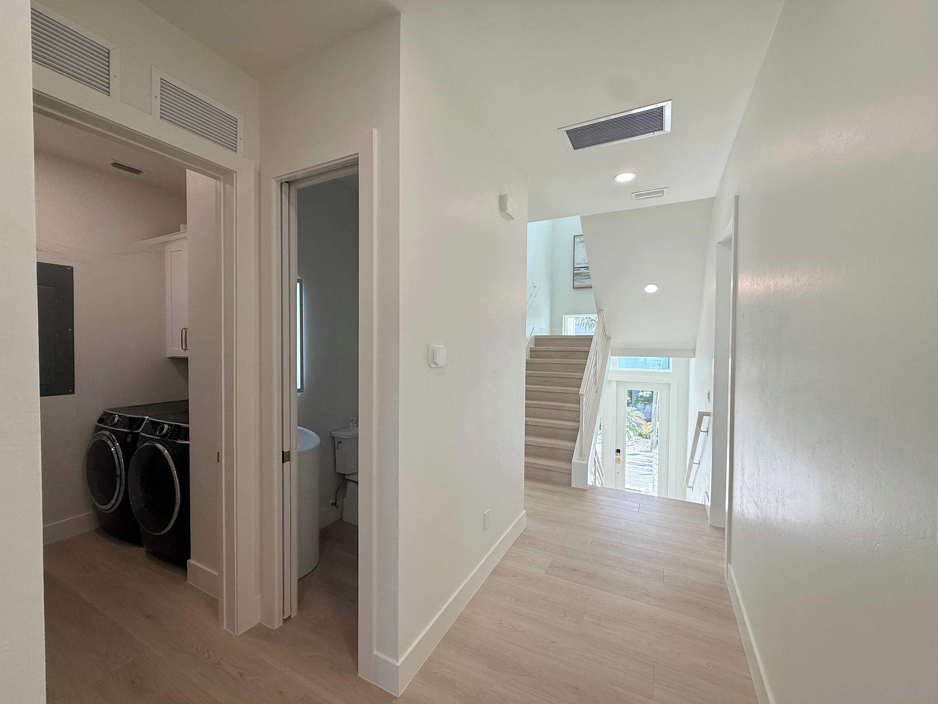 A hallway with a laundry area, a bathroom, and a staircase leading to an upper floor.