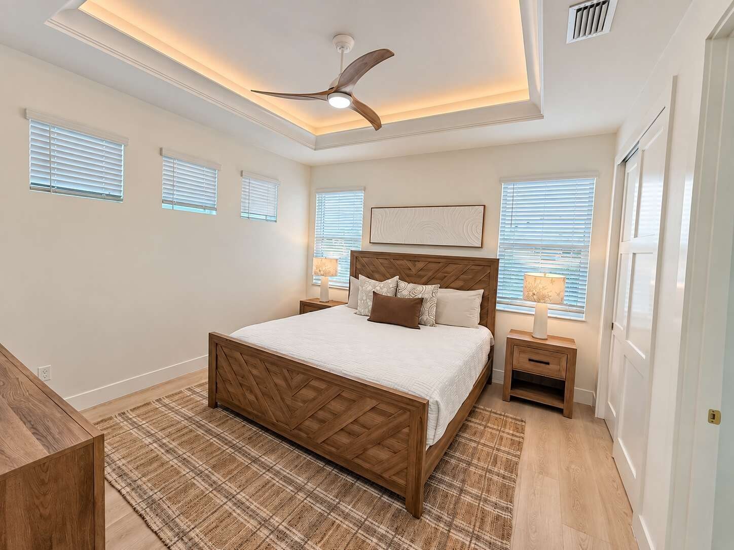 A bedroom with a wooden bed, a ceiling fan, bedside lamps, and a plaid rug.