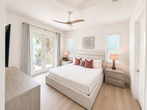 A bedroom with a large bed, two bedside tables, a ceiling fan, and a view through a sliding glass door. - Drift House · 2026 Luxury 6 King Suites Boat Dock (Fort Myers Beach)
