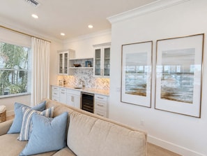 A modern kitchen with white cabinetry, a marble backsplash, and a built-in oven. There is a beige sofa with blue pillows in the living area, and two framed pictures on the wall. - Drift House · 2026 Luxury 6 King Suites Boat Dock (Fort Myers Beach)