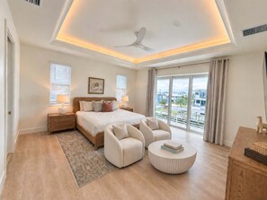A modern bedroom with a large bed, two bedside tables, a ceiling fan, and a view of the outside. - Drift House · 2026 Luxury 6 King Suites Boat Dock (Fort Myers Beach)
