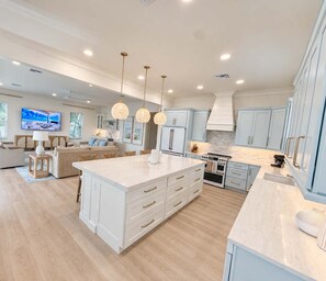 A modern kitchen with a large island, light blue cabinets, and pendant lighting. - Drift House · 2026 Luxury 6 King Suites Boat Dock (Fort Myers Beach)