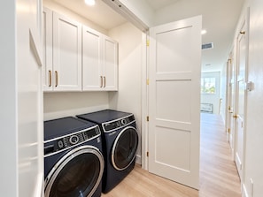 A laundry room with two front-loading washing machines, white cabinets with gold handles, and a white door. - Drift House · 2026 Luxury 6 King Suites Boat Dock (Fort Myers Beach)